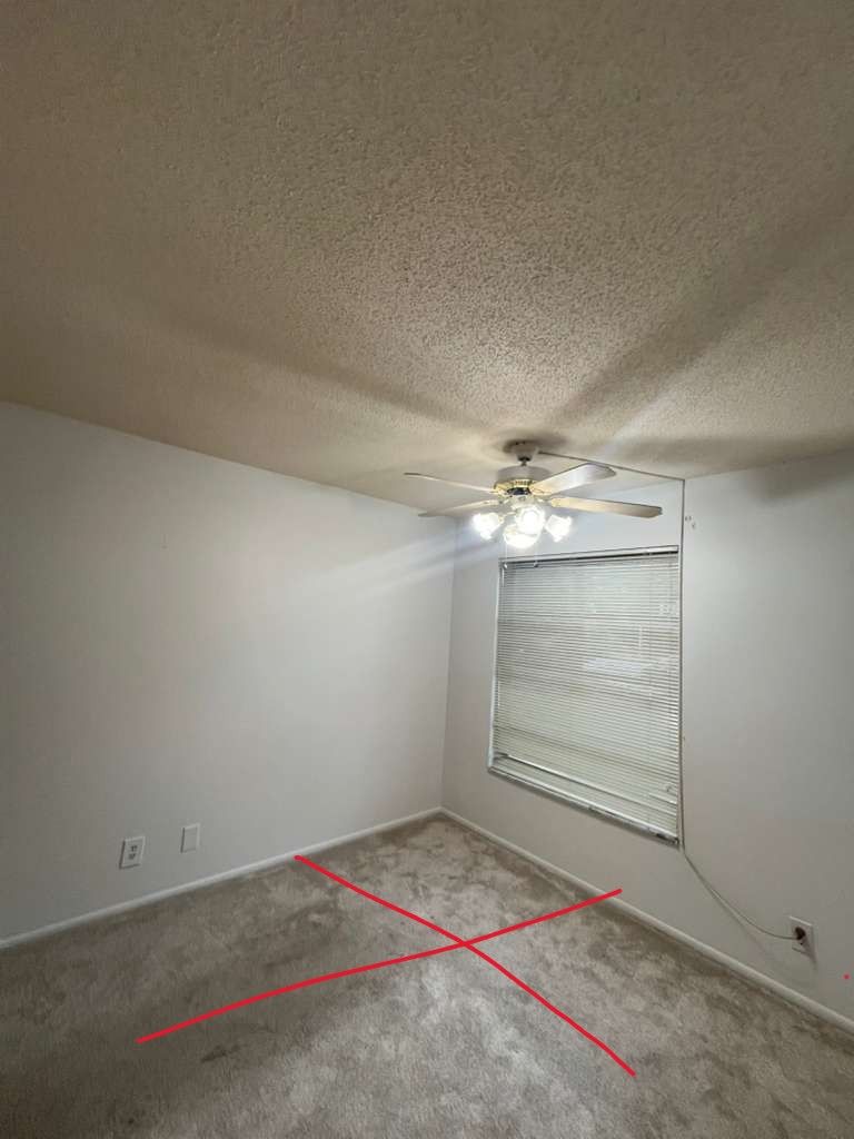 A carpeted bedroom with a red X on the floor
