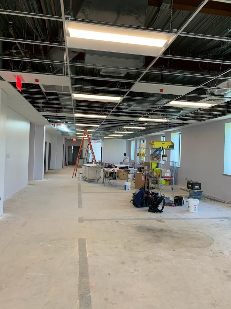 Empty office under construction with exposed ceiling, ladders, and tools on the floor