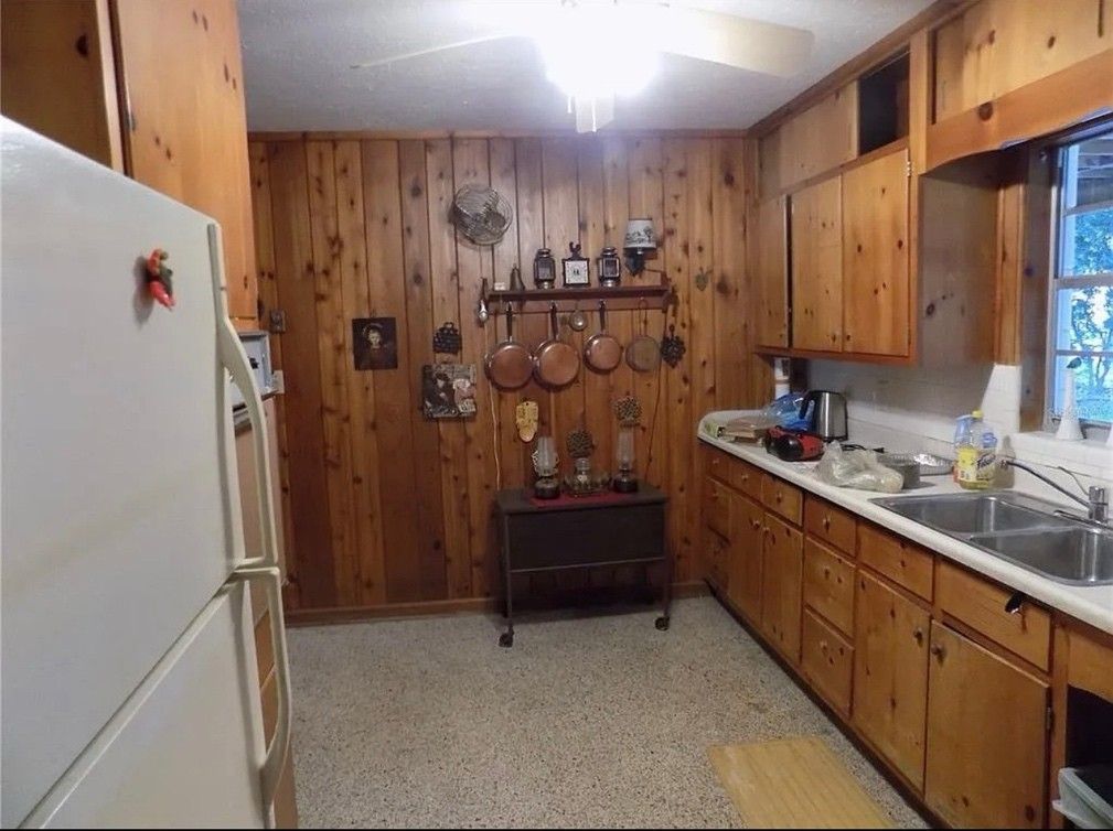 Kitchen with wood paneling, cabinets, and appliances. Copper pots hang on the wall.