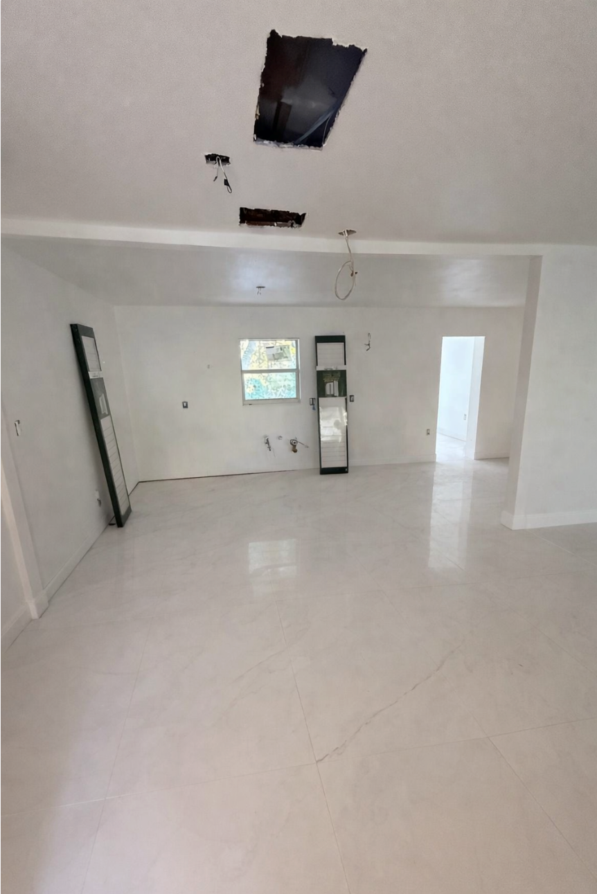 Interior of a room under construction with a smooth, light-colored floor, bare walls, and a damaged ceiling.
