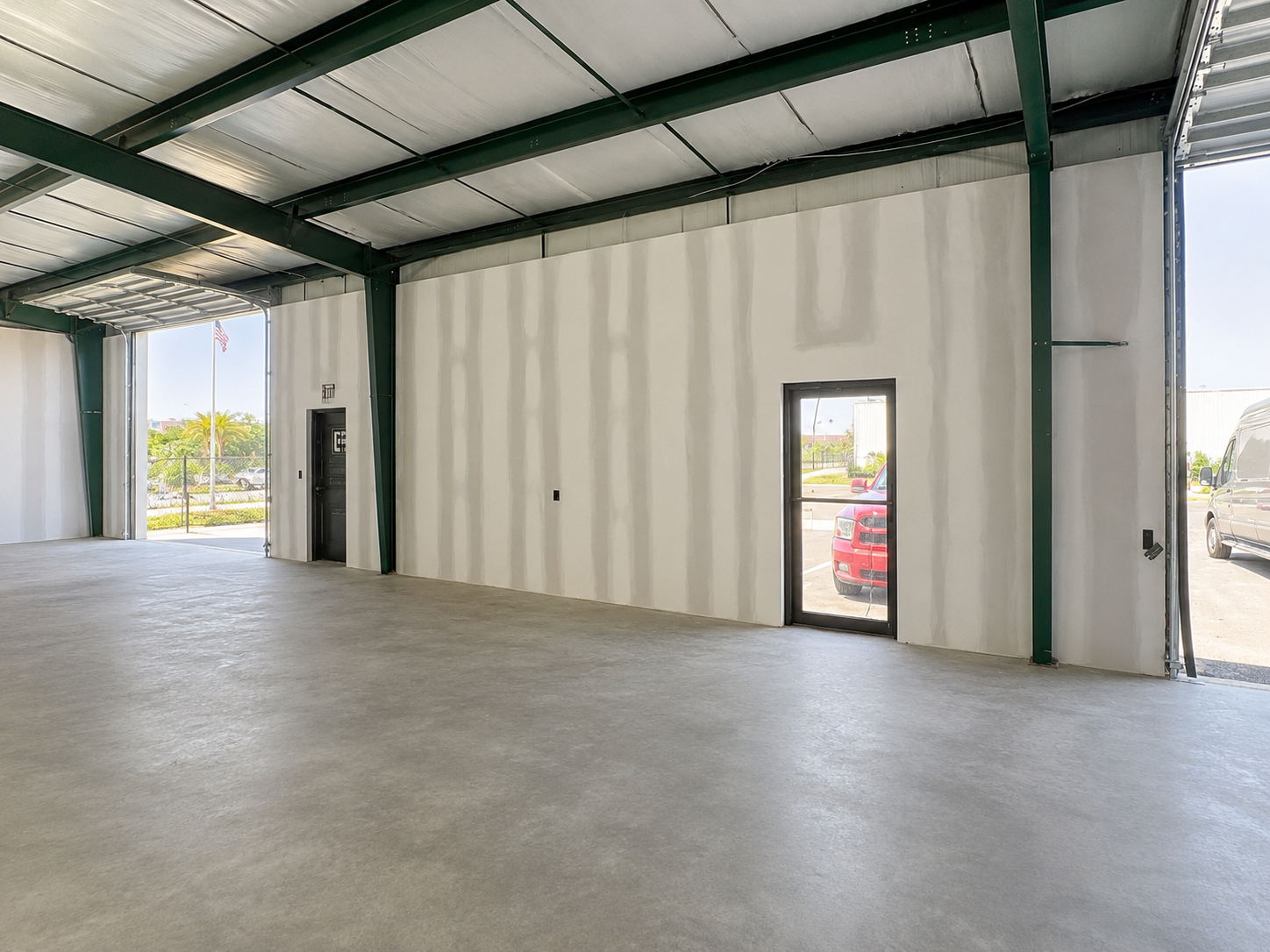 Empty industrial warehouse interior with concrete floor, white walls, and green steel beams.