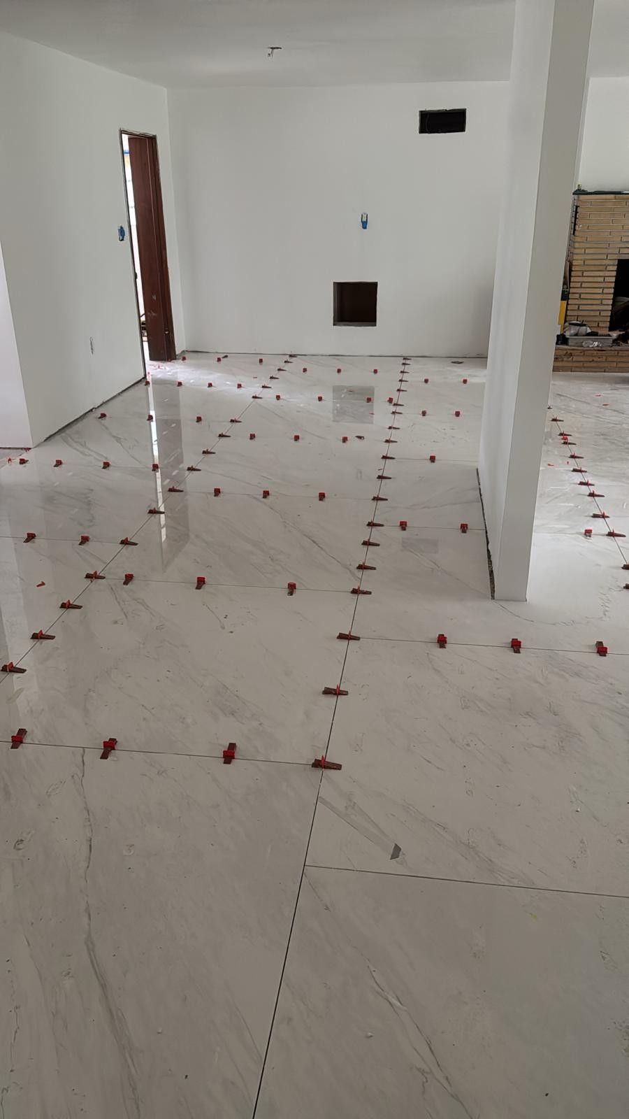 Newly installed tile floor with red leveling clips, a white room, and a partially open door.