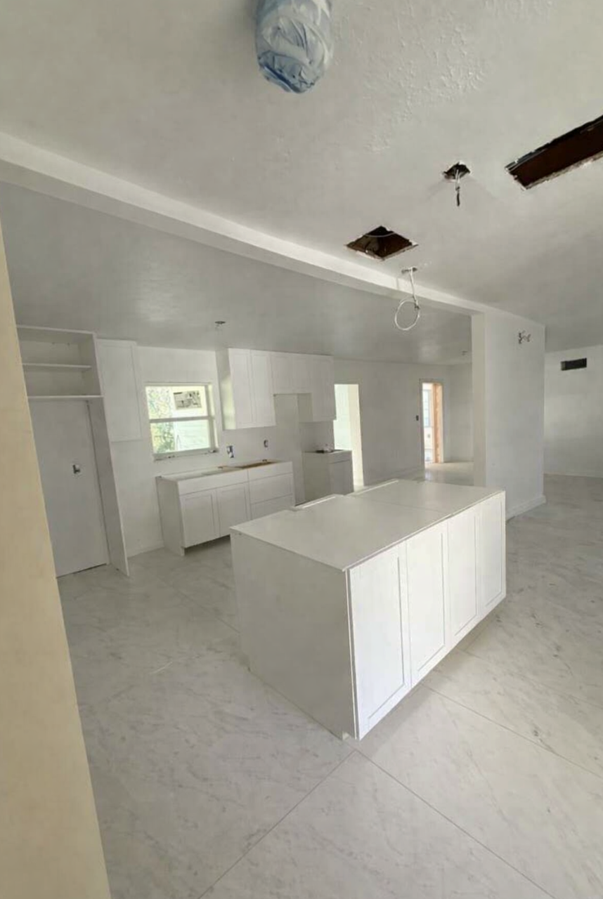 Interior view of a kitchen under construction, with white cabinets, island, and walls, covered in protective wrap.