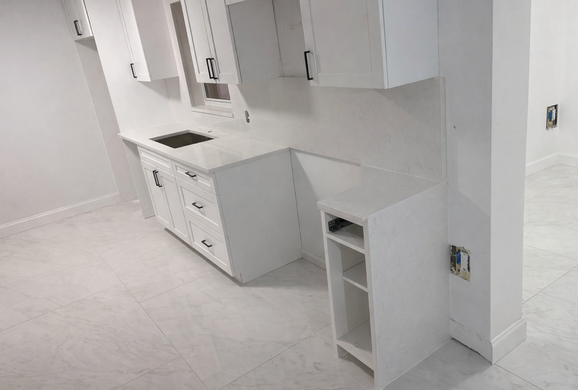 White kitchen cabinets with black hardware and a light countertop in a corner.