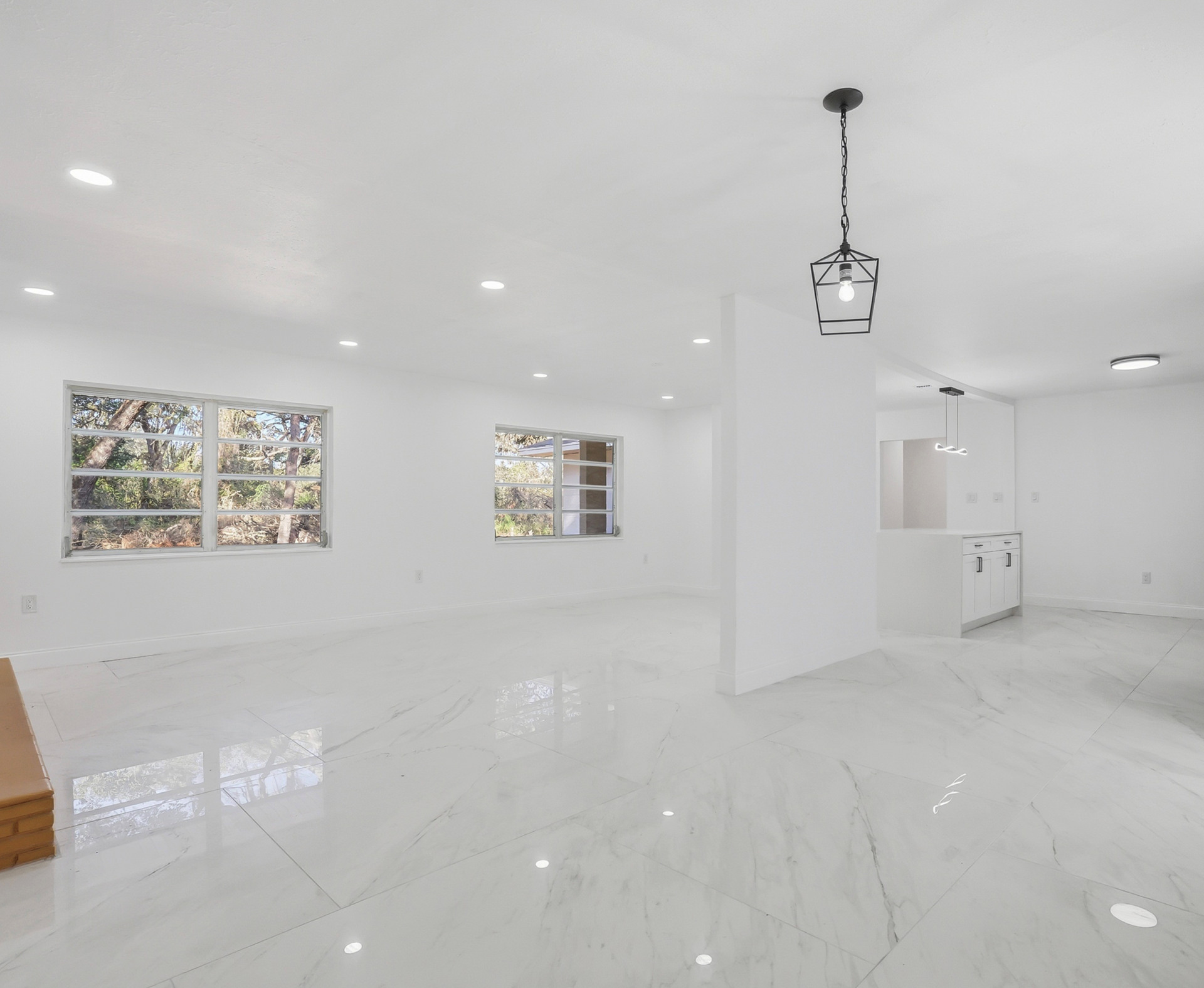 Bright, white, empty room with large windows and marble floors. A modern pendant light hangs from the ceiling.