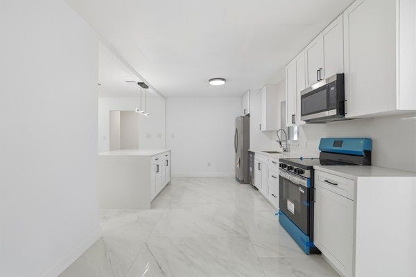 White modern kitchen with cabinets, appliances, and a marble floor.