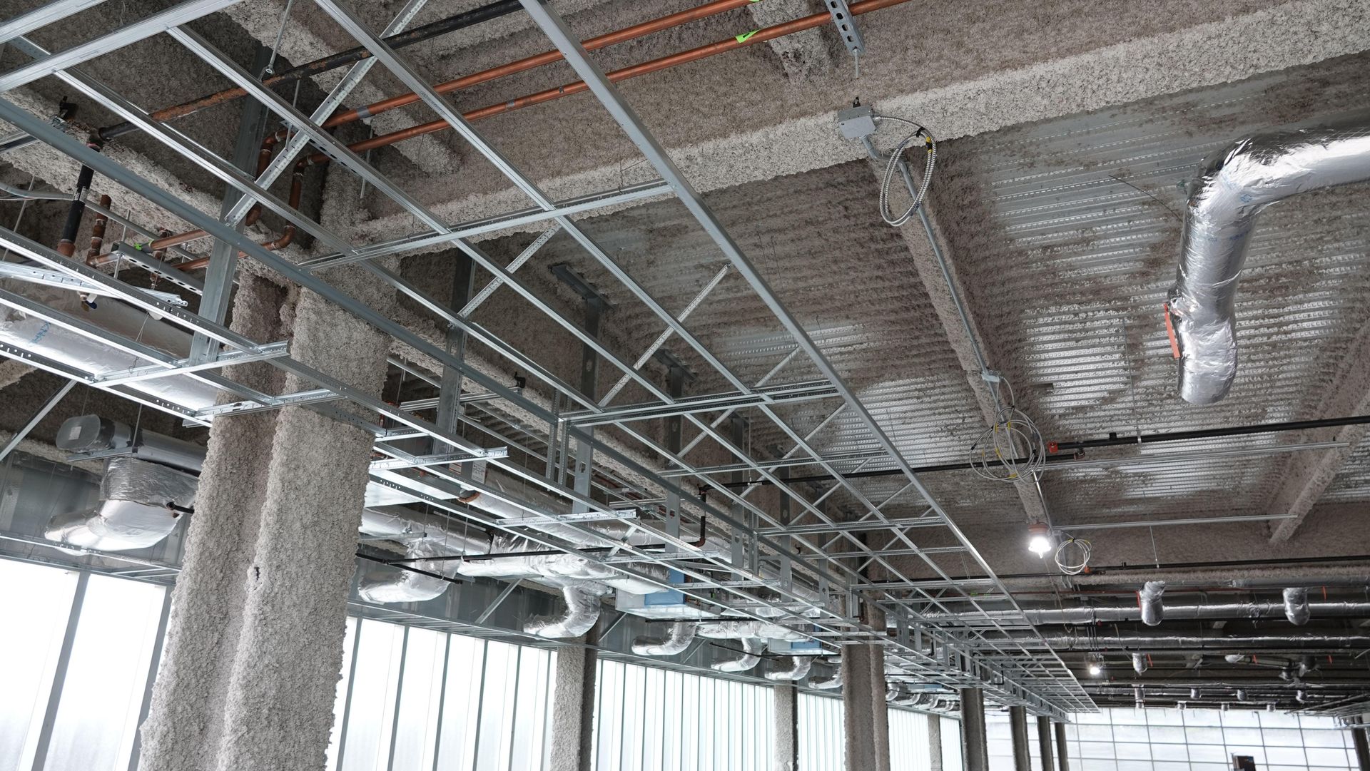 Exposed ceiling ductwork and lighting in an unfinished building interior with windows along one side