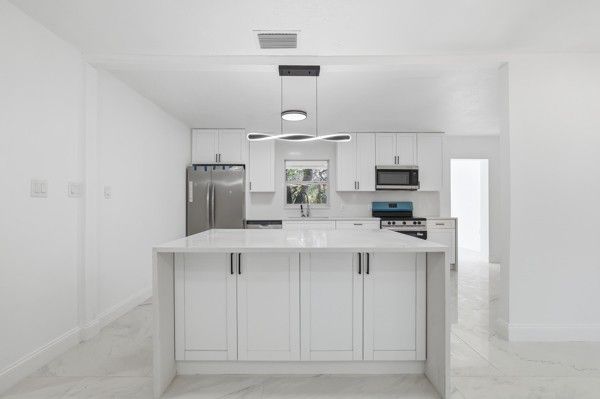 White kitchen with island, stainless steel appliances, and modern lighting.