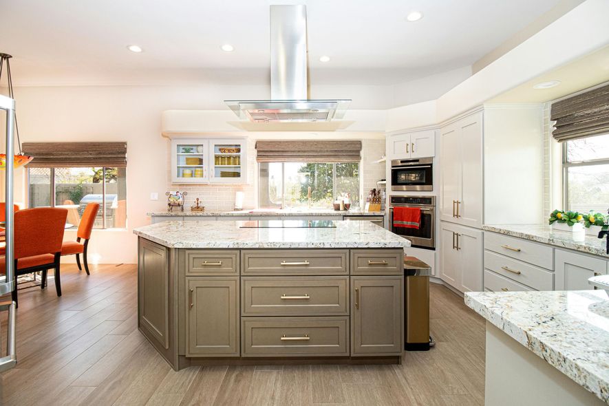 Spacious kitchen with gray island, white cabinets, granite countertops, and light wood flooring.