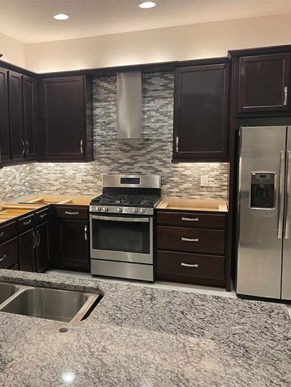 Kitchen with dark brown cabinets, stainless steel appliances, light granite countertops, and stone backsplash.