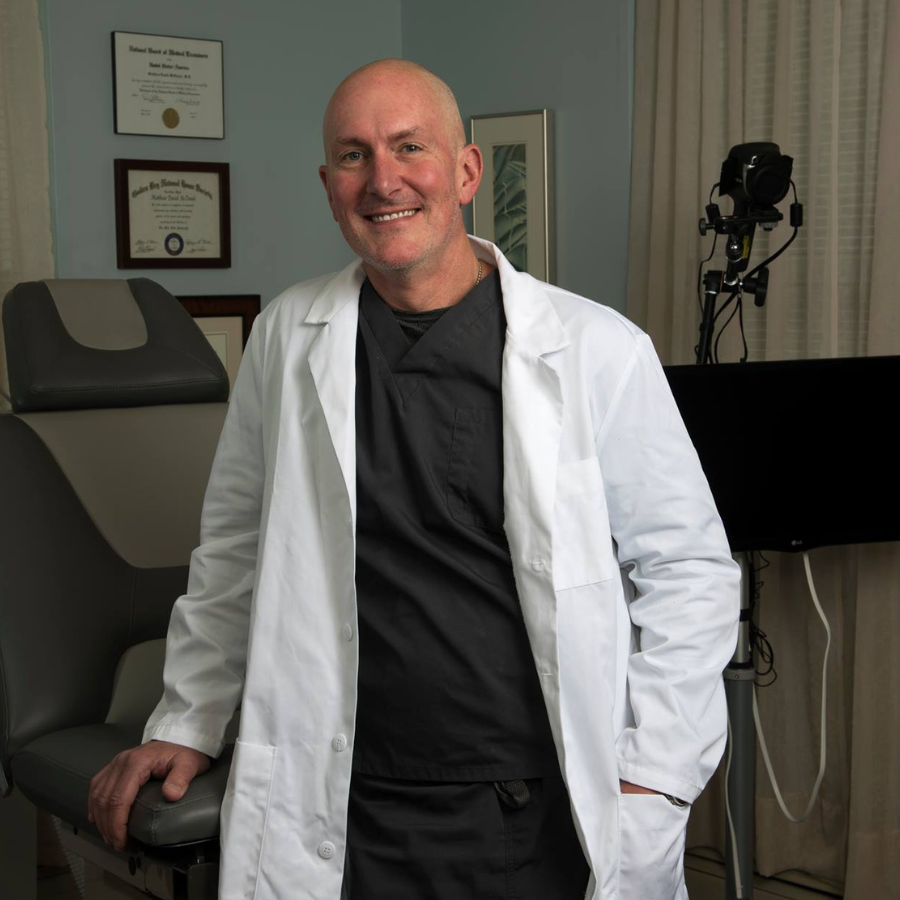 A bald man wearing a white lab coat and a black shirt