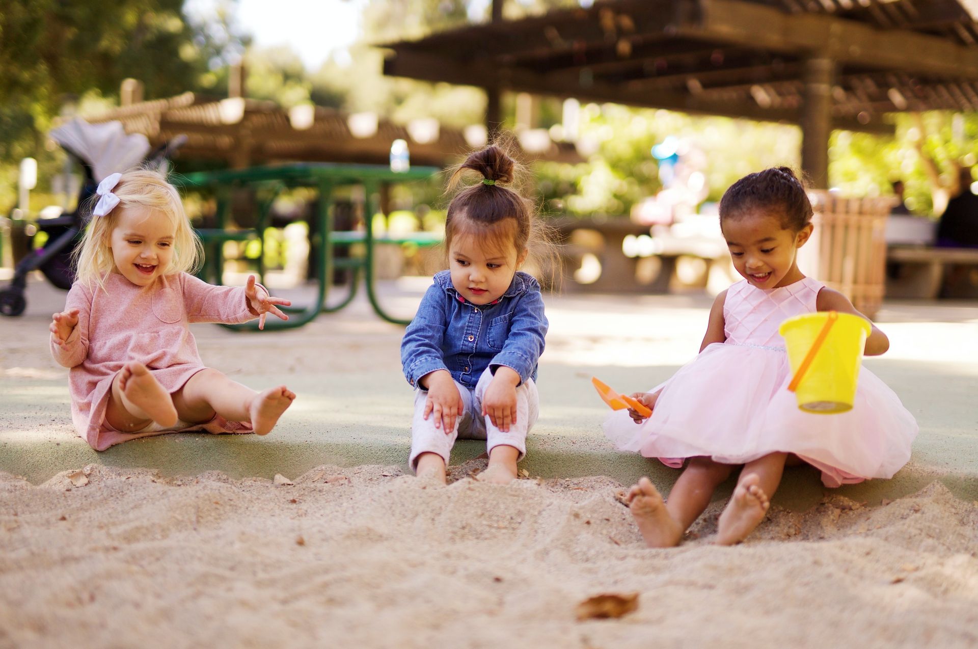 Three little girls are sitting in the sand at a playground.