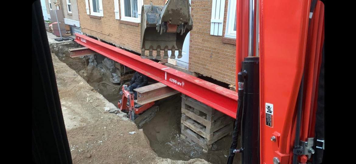 Une excavatrice rouge déplace un bâtiment dans un trou.