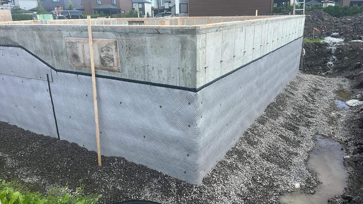 Fondations en béton avec revêtement protecteur, entourées de gravier et de terre.