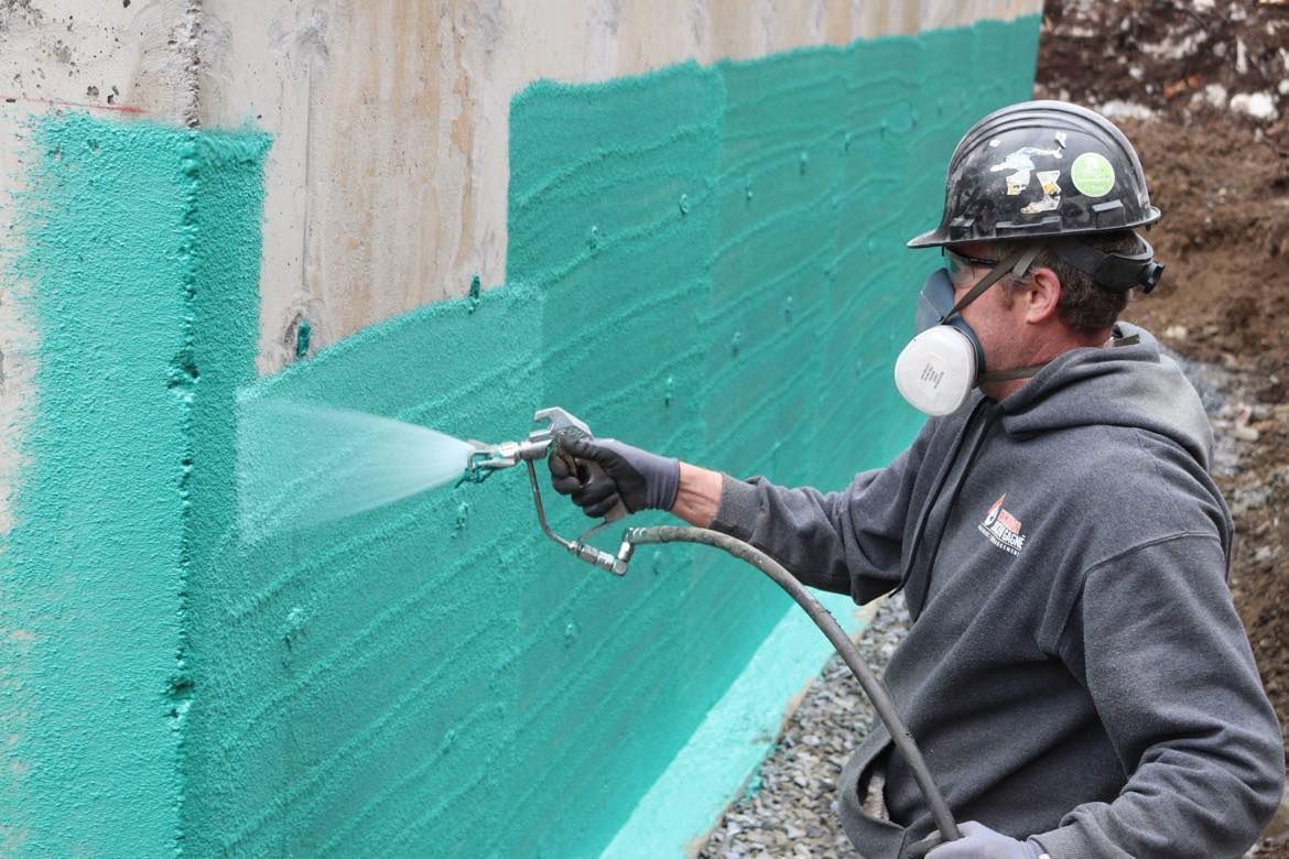 Un homme pulvérise de la peinture verte sur un mur en béton.