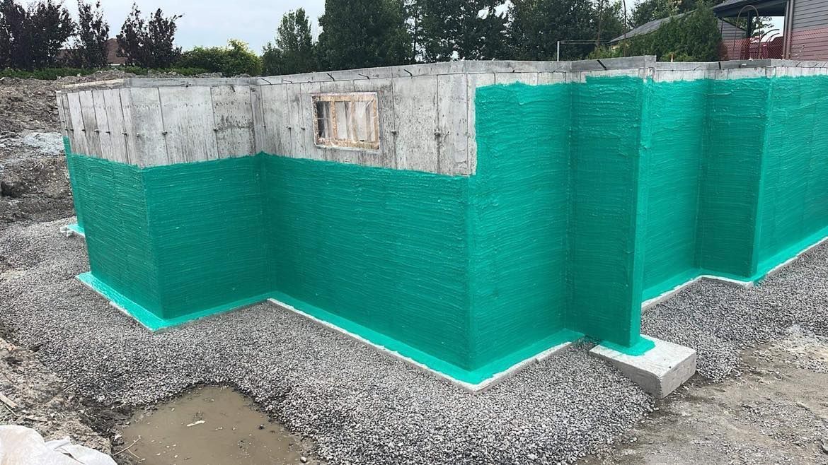 Fondations en béton recouvertes d'un matériau d'étanchéité vert, sur une base de gravier.