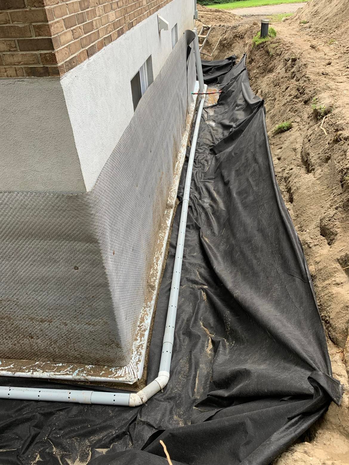 Étanchéité des fondations avec tuyau de drainage et tissu noir.