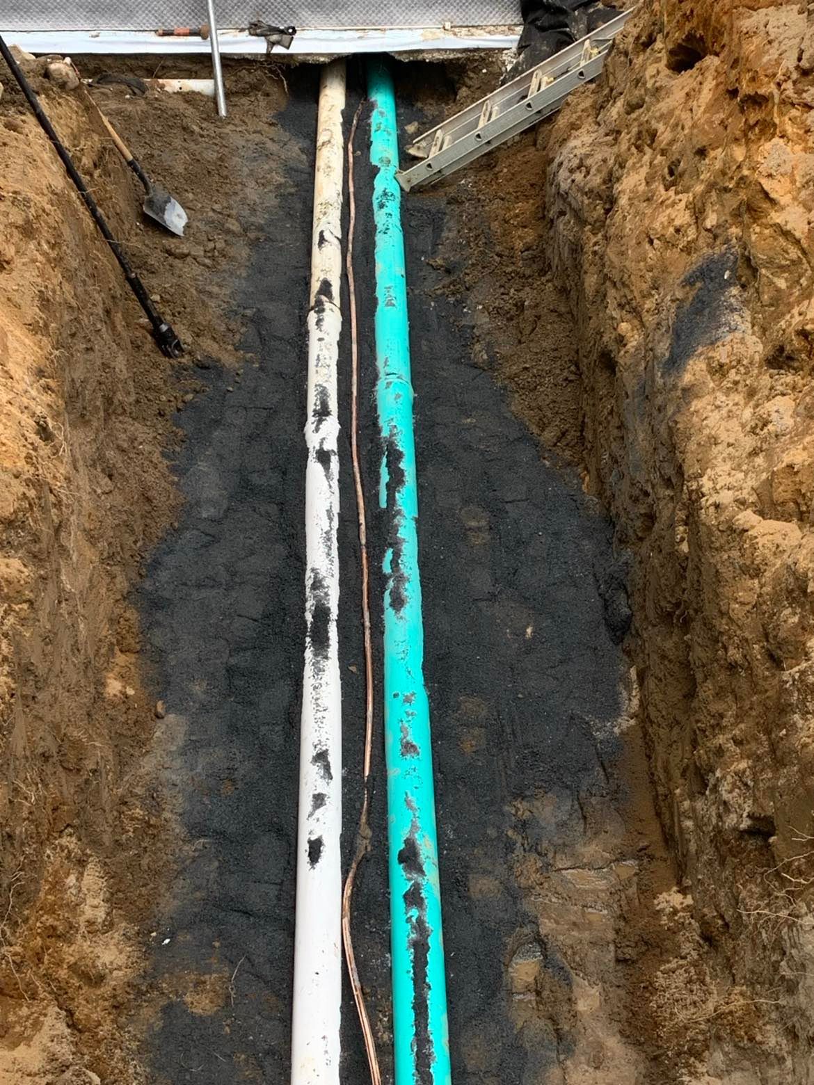 Un tuyau vert et blanc est en train d'être installé dans une tranchée.