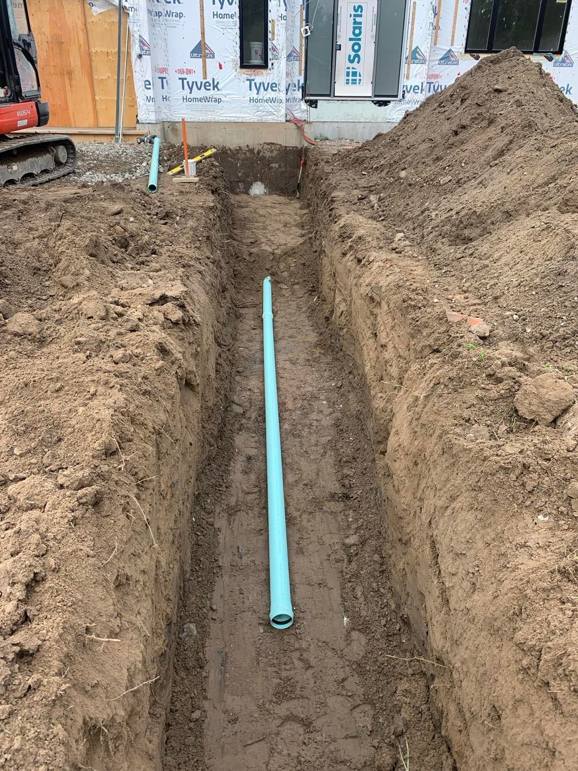 Un tuyau vert est en train d'être installé dans une tranchée dans la terre.