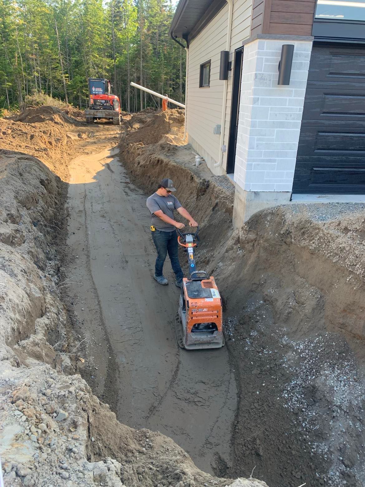 Un homme utilise une machine pour niveler un chemin de terre devant une maison.