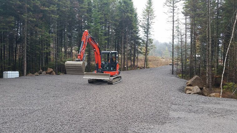 Une excavatrice circule sur une route de gravier dans les bois.
