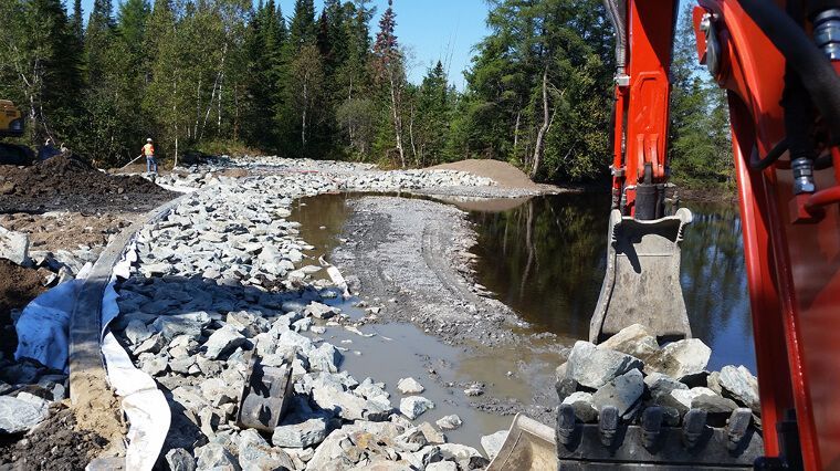 Une excavatrice rouge déplace des roches dans une rivière.