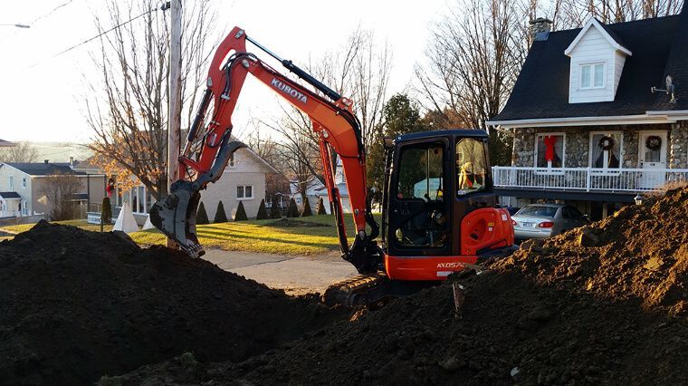 Une excavatrice creuse un trou devant une maison.
