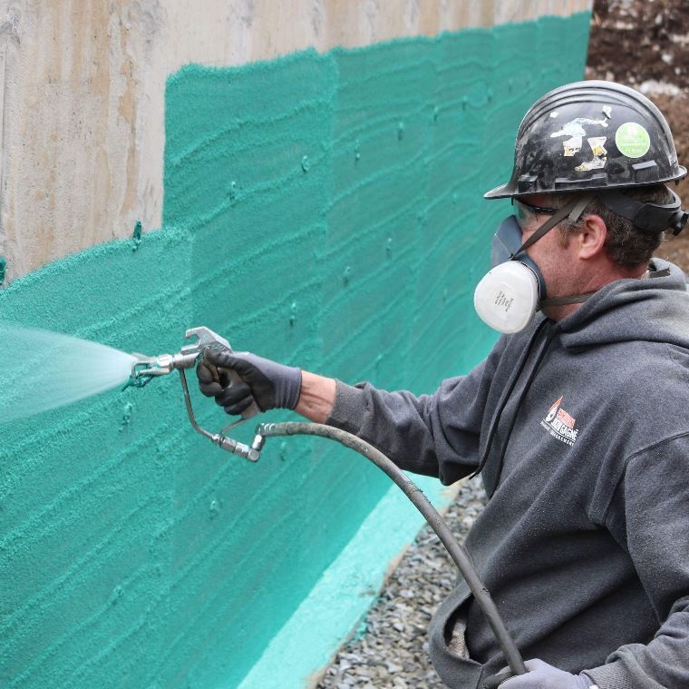 Un homme portant un casque et un masque pulvérise de la peinture verte sur un mur