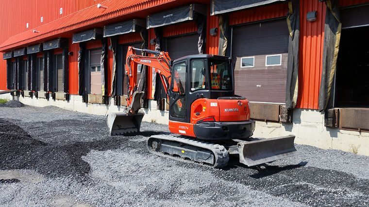Une pelleteuse orange est garée devant un quai de chargement.