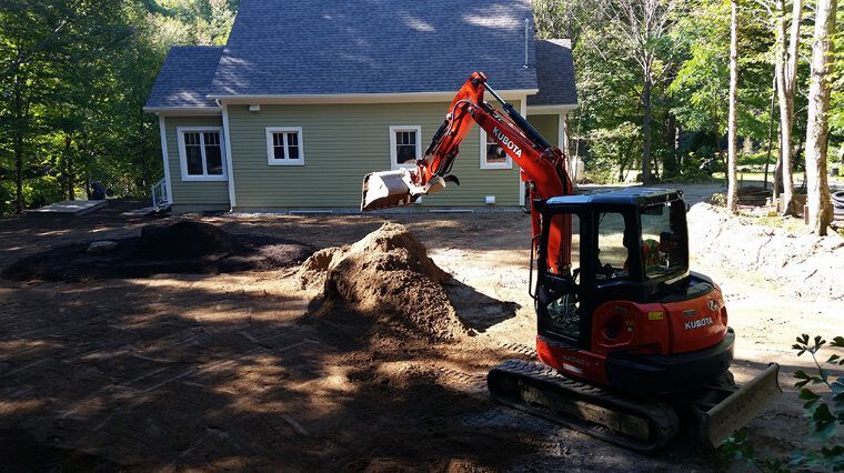 Une excavatrice creuse un tas de terre devant une maison.