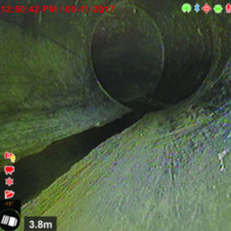 À l'intérieur d'un tuyau, un orifice rond laisse s'écouler un filet d'eau. Couleur gris-vert. L'horodatage et l'indicateur de distance sont visibles.