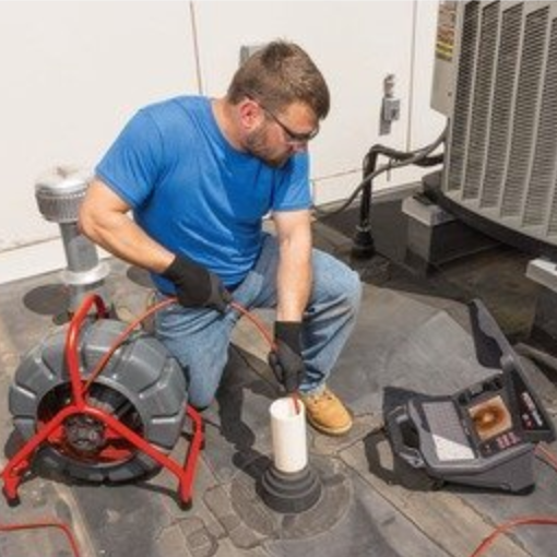 Un homme est assis par terre et utilise une caméra de drainage.