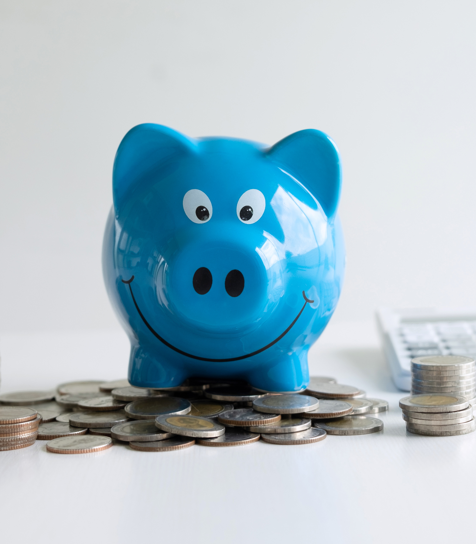 Blue piggy bank sitting on a pile of coins, calculator in background.