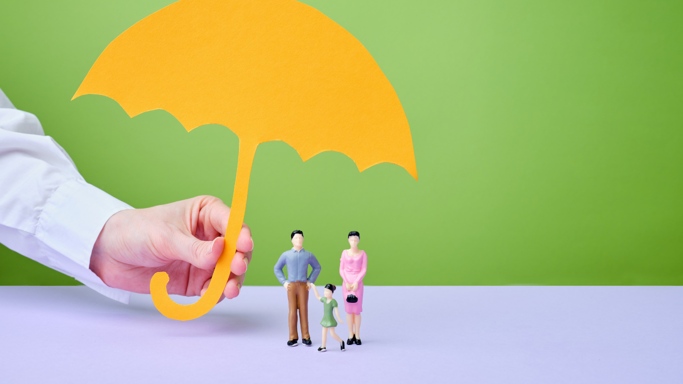 Hand holding a yellow paper umbrella over a miniature family; green background.