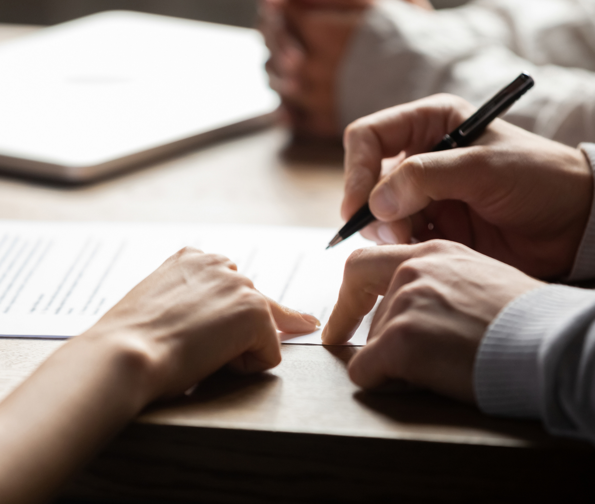 Hands signing a document on a table, one finger pointing to the signature line.