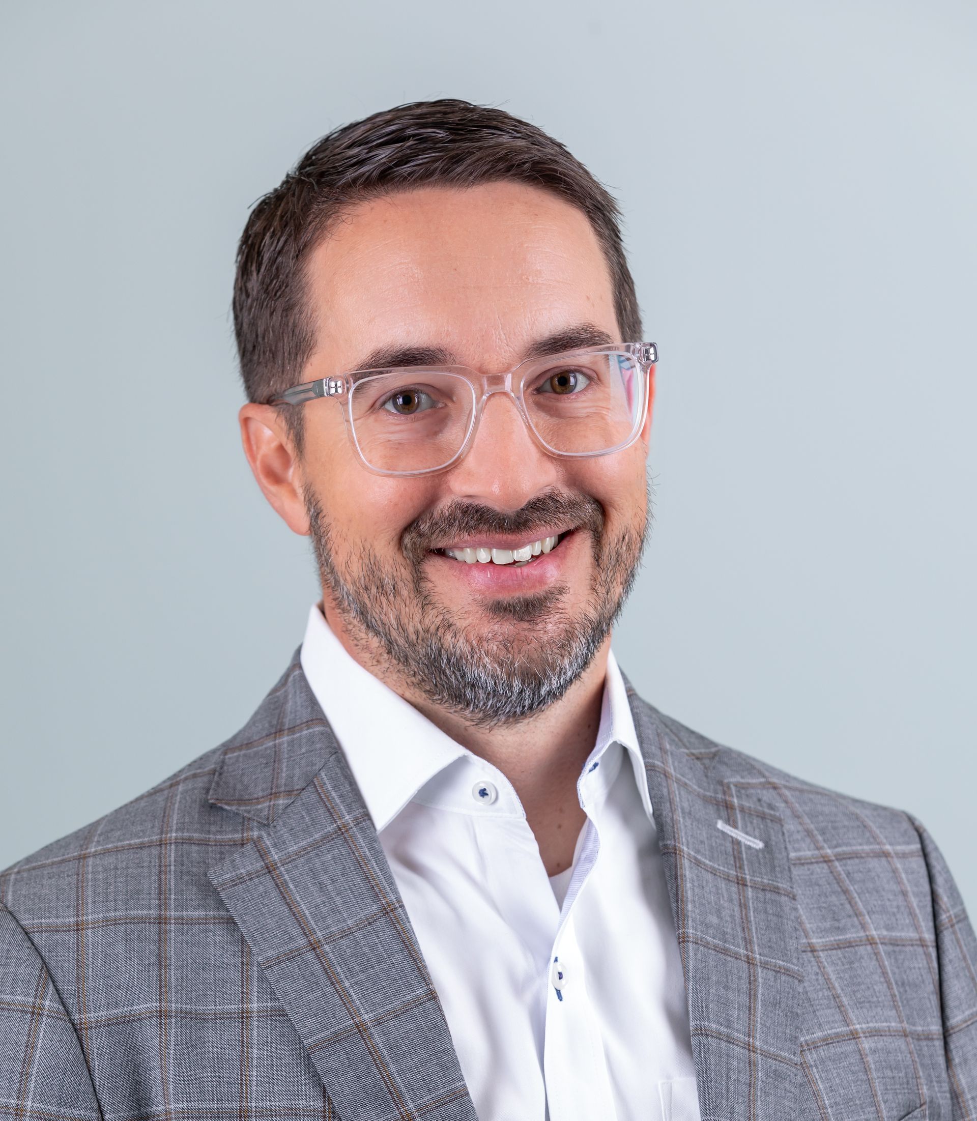 A man wearing glasses and a suit is smiling for the camera.