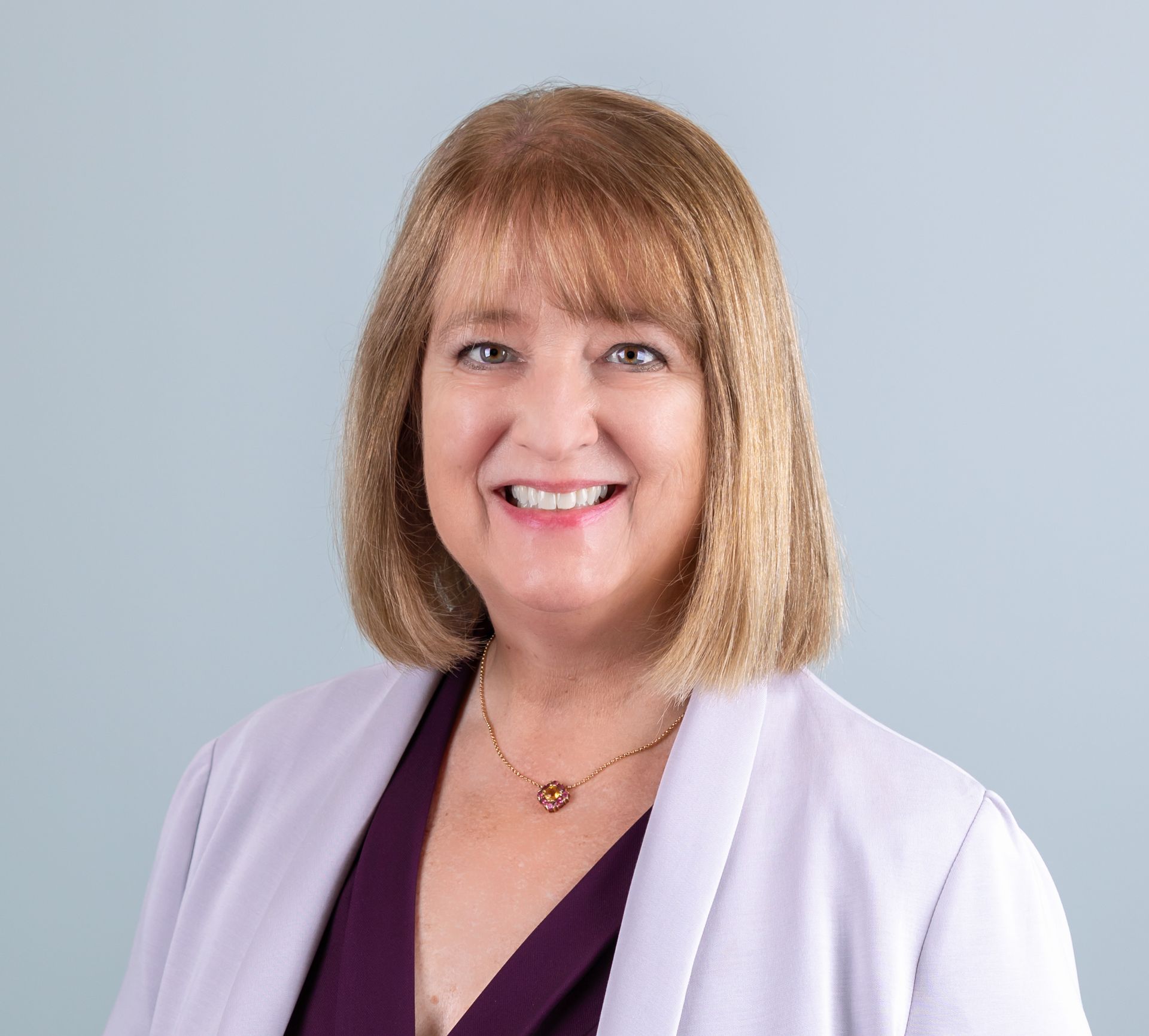 A woman wearing a purple shirt and a purple jacket is smiling for the camera.