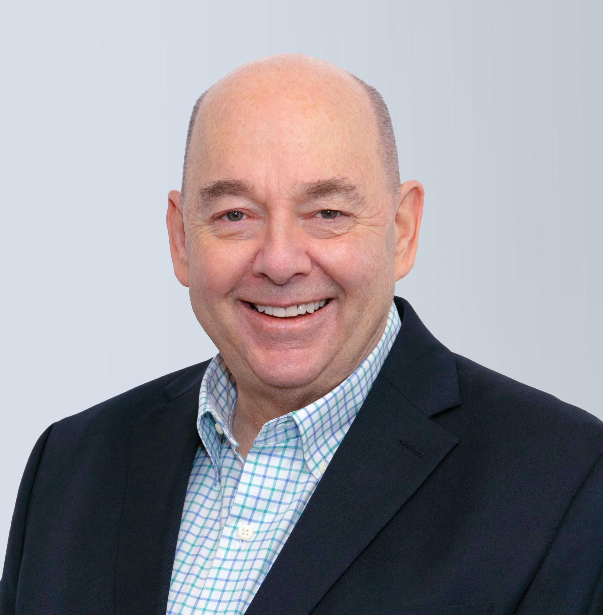 A man in a suit and plaid shirt is smiling for the camera.