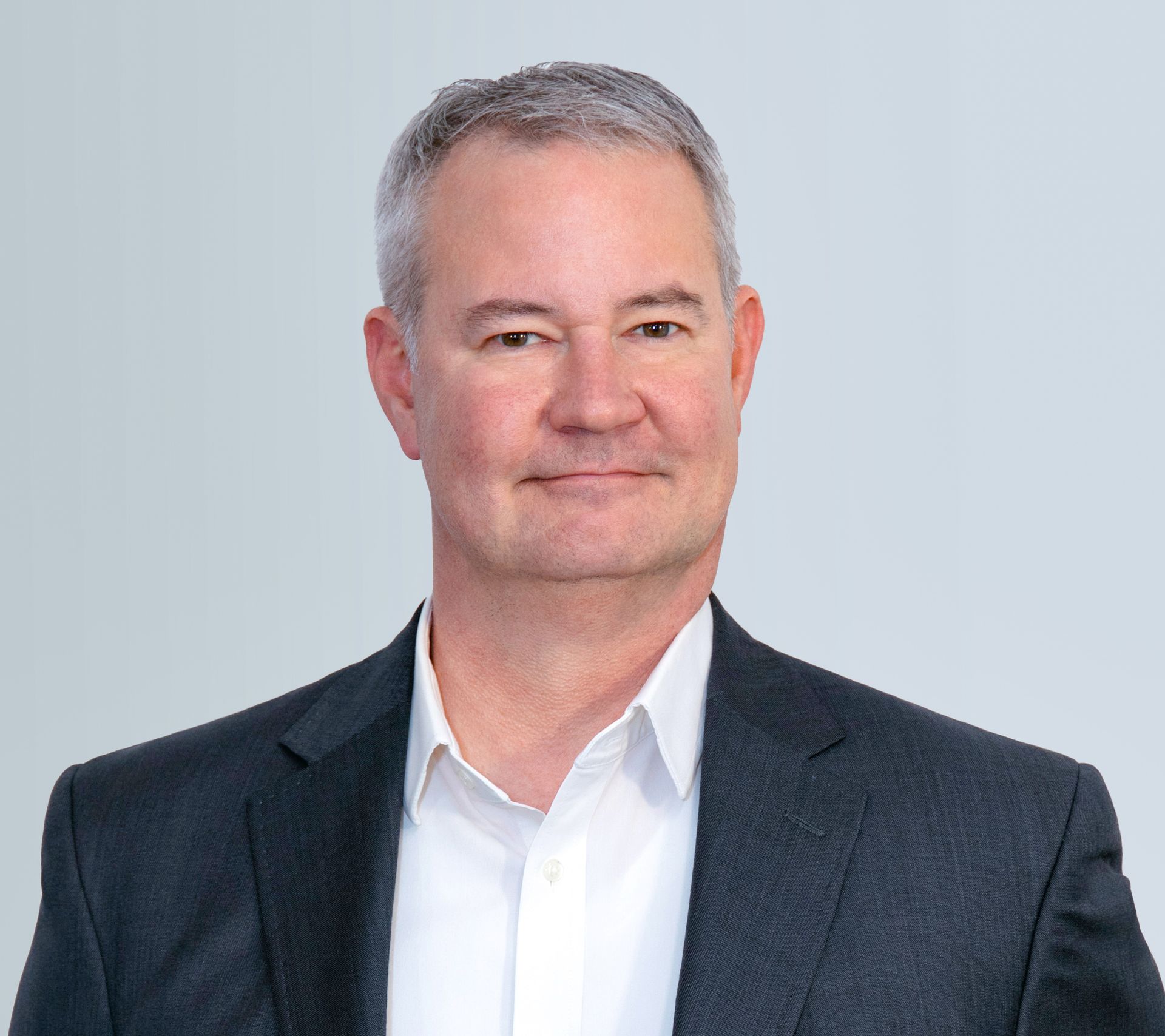 A man in a suit and white shirt is smiling for the camera.