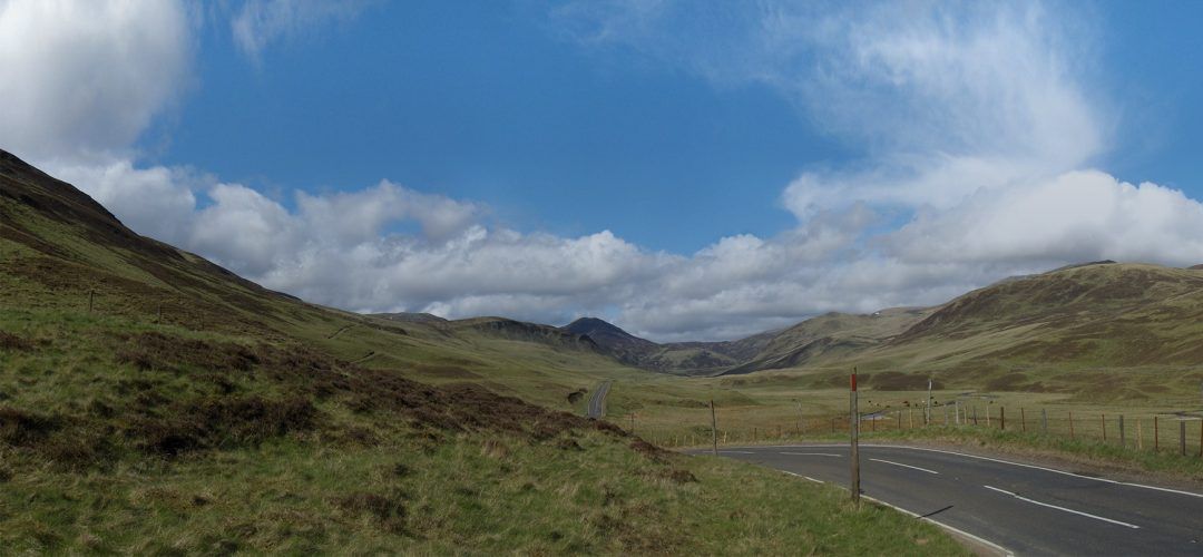 A road going through a valley with mountains in the background.