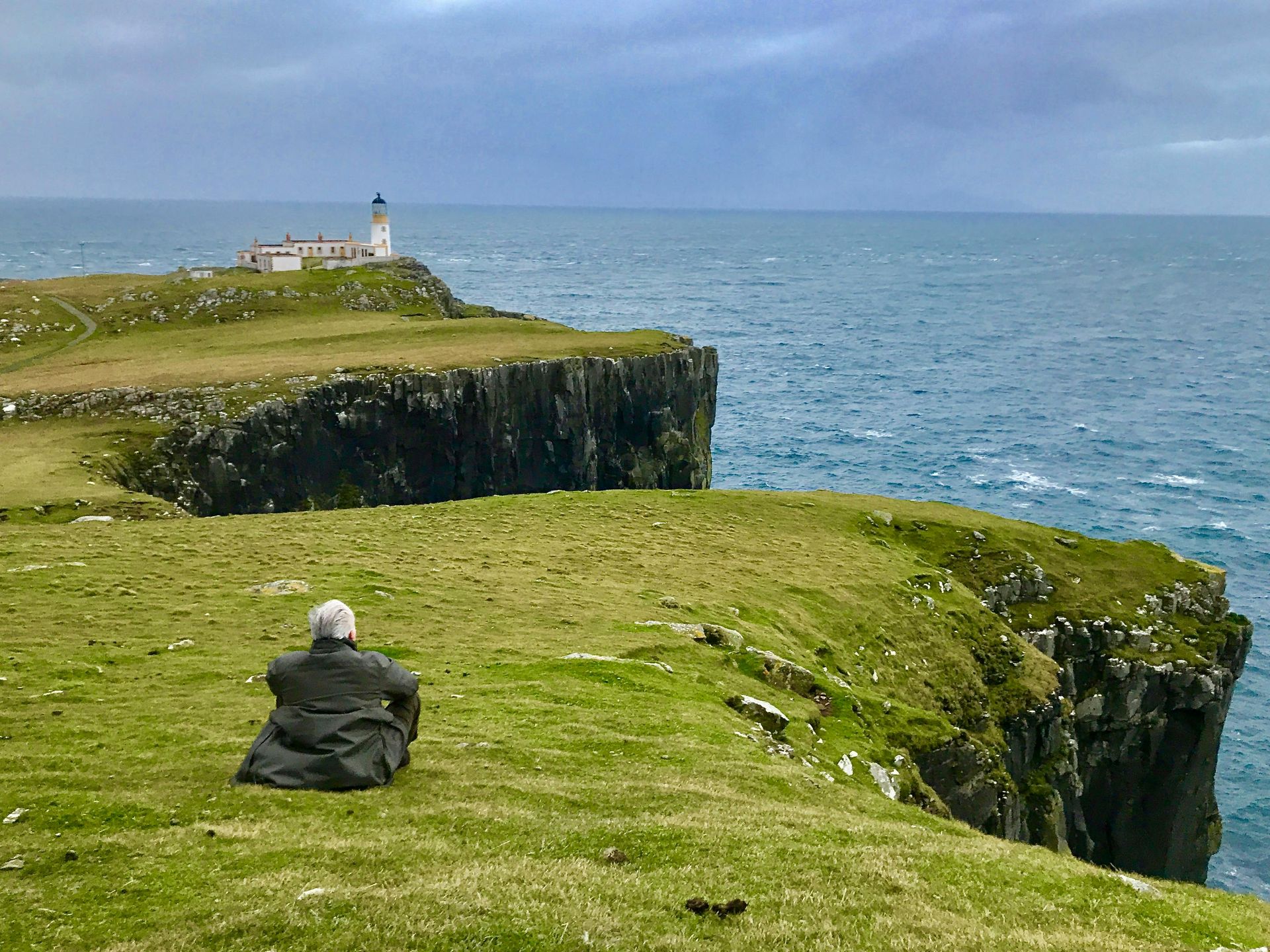 A man is sitting on the edge of a cliff overlooking the ocean.