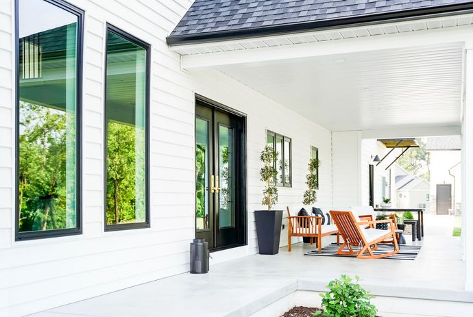 A white house with a black roof and a porch with chairs and tables.