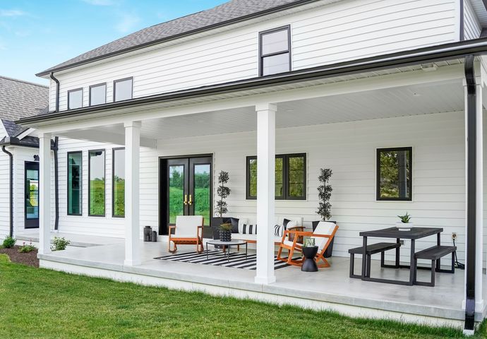 A white house with a large porch and patio furniture.