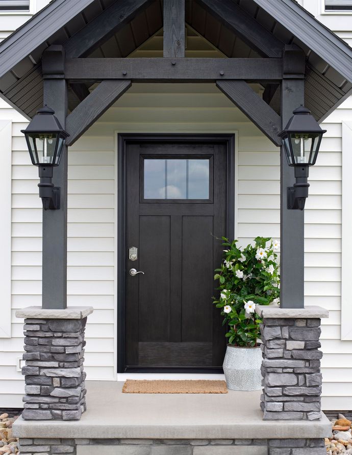 The front door of a white house with a black door and a stone porch.