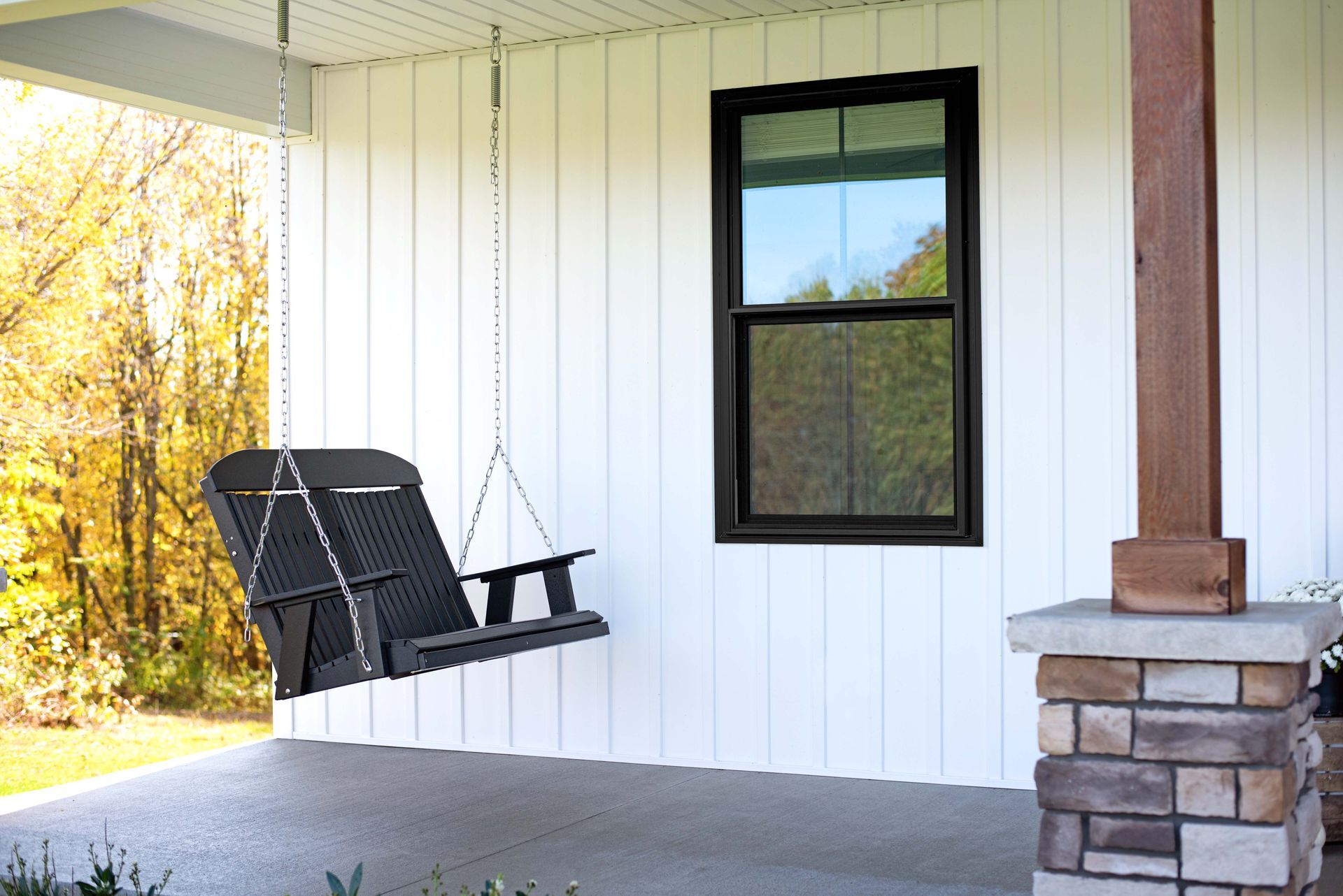 A porch with a swing hanging from the ceiling and a window.