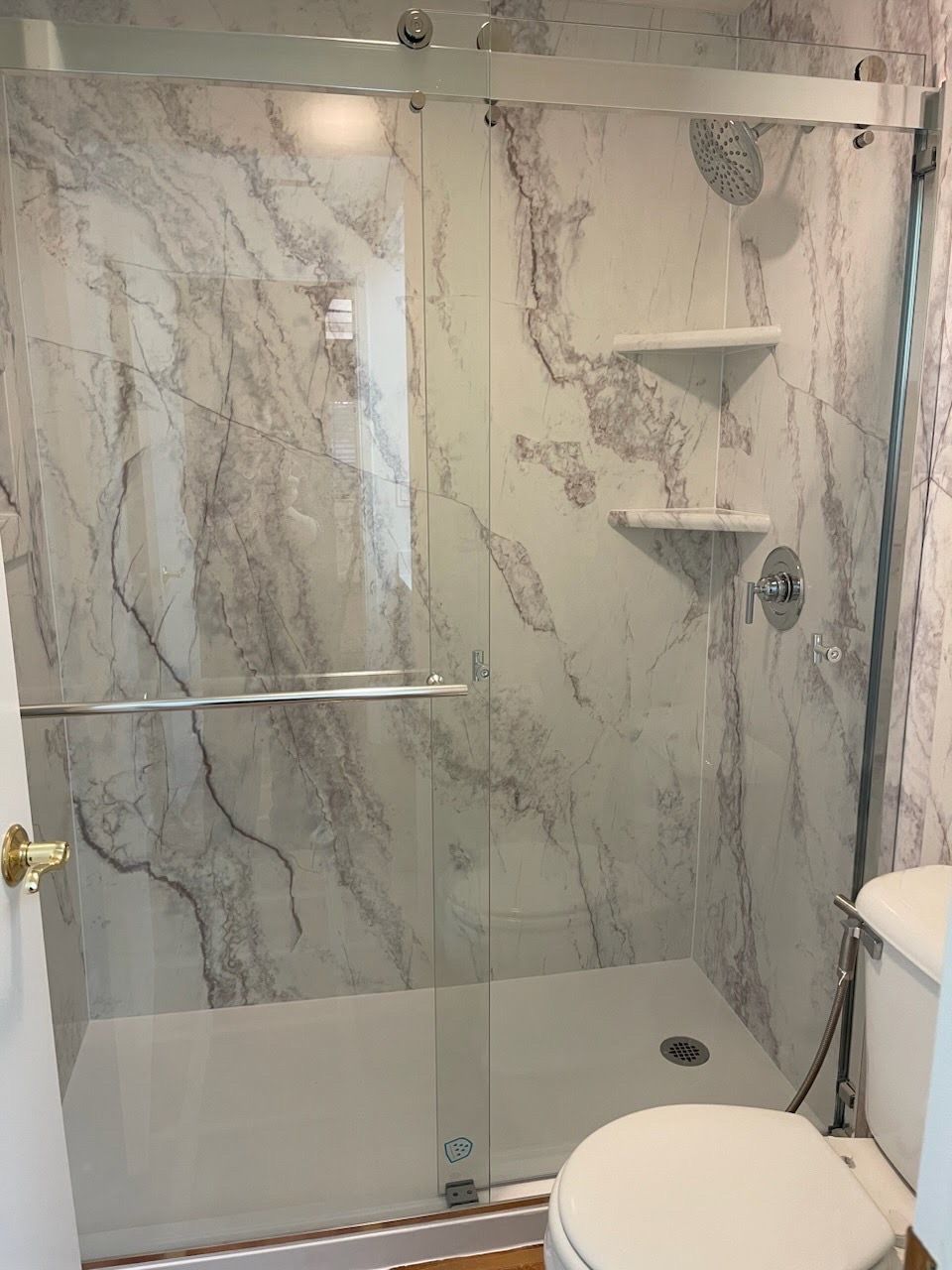 A bathroom with a toilet , shower , and marble walls.