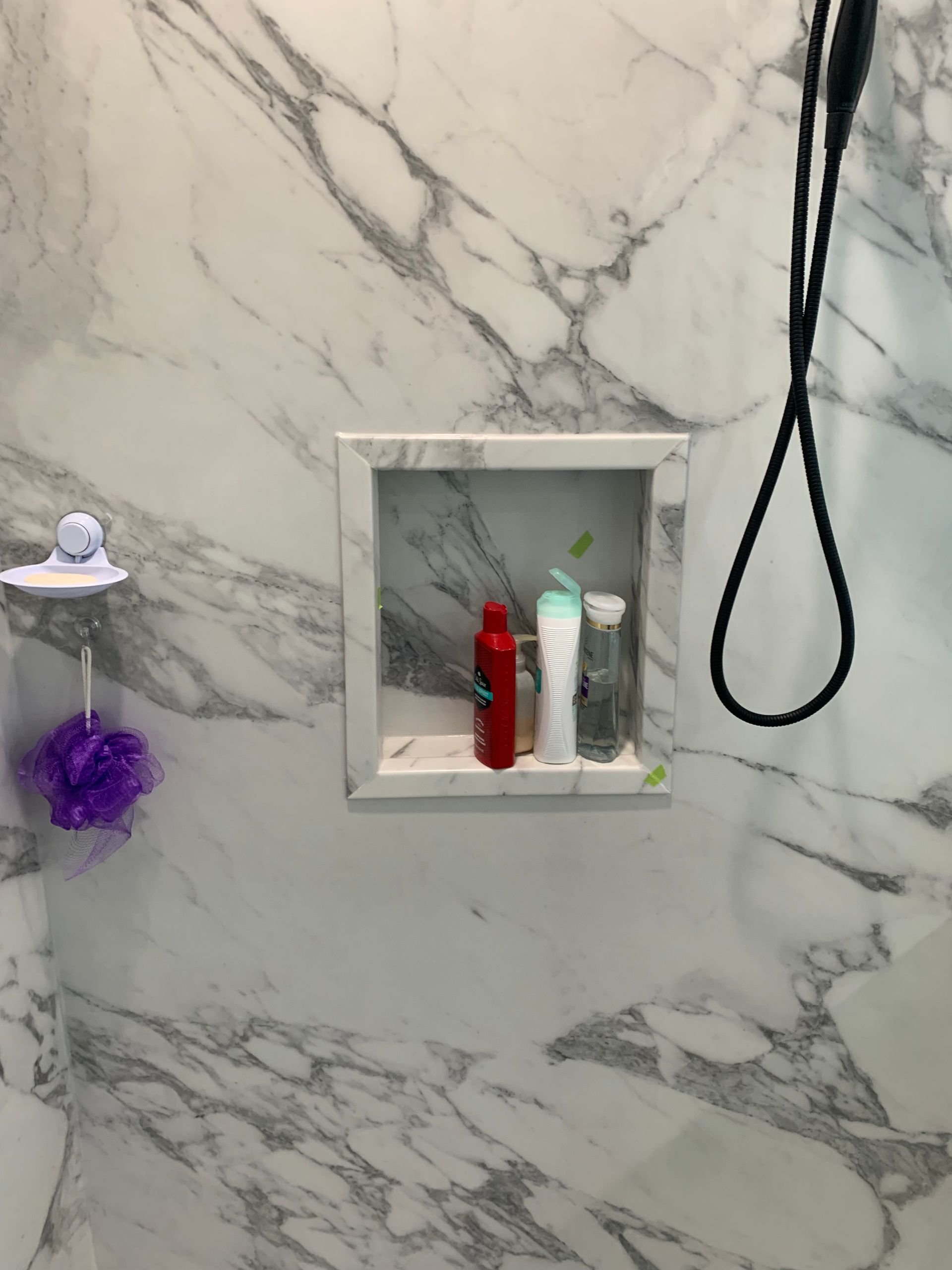 A bathroom with a shower head and a shelf with bottles on it