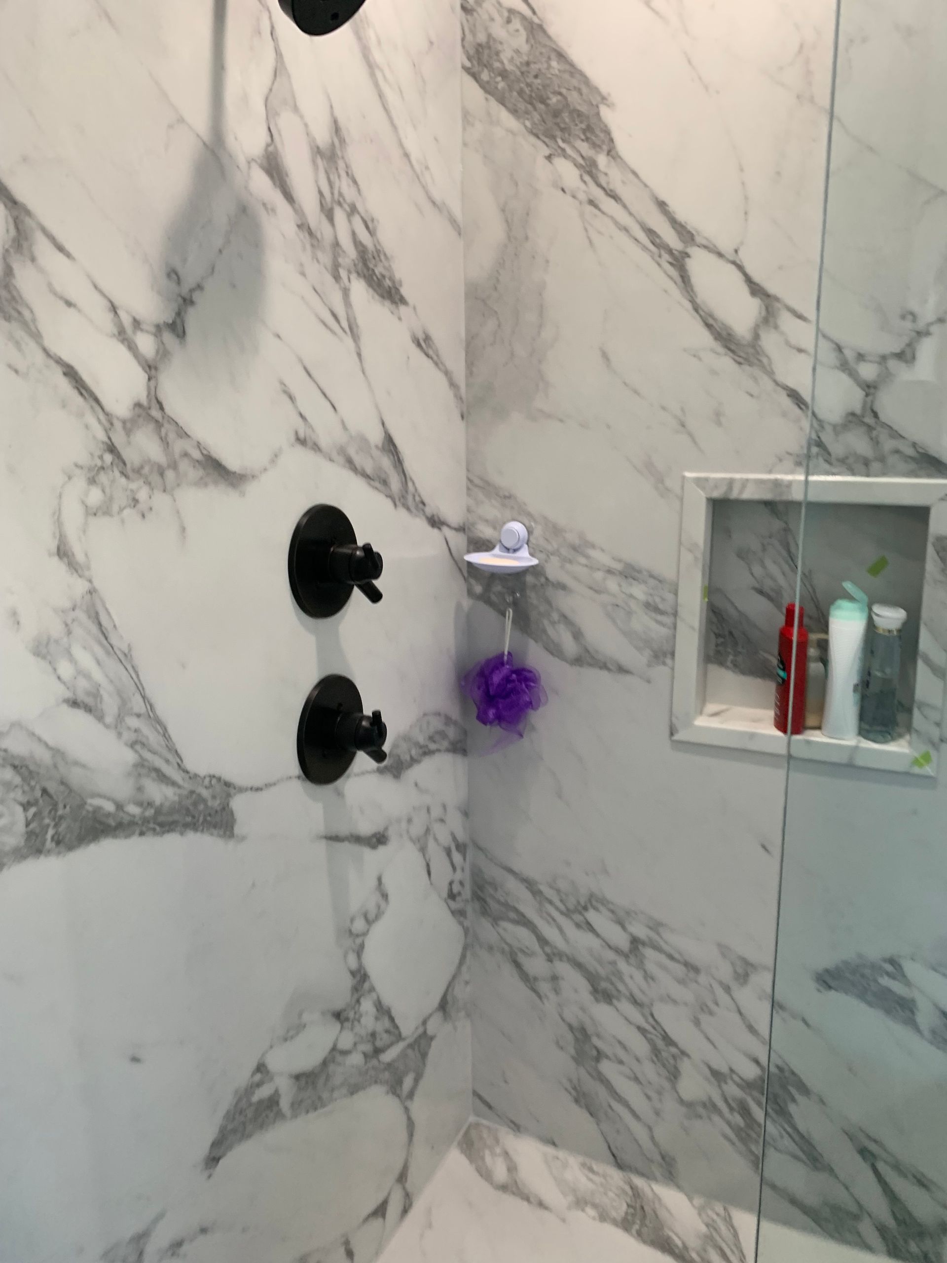 A shower with a marble wall and a black shower head