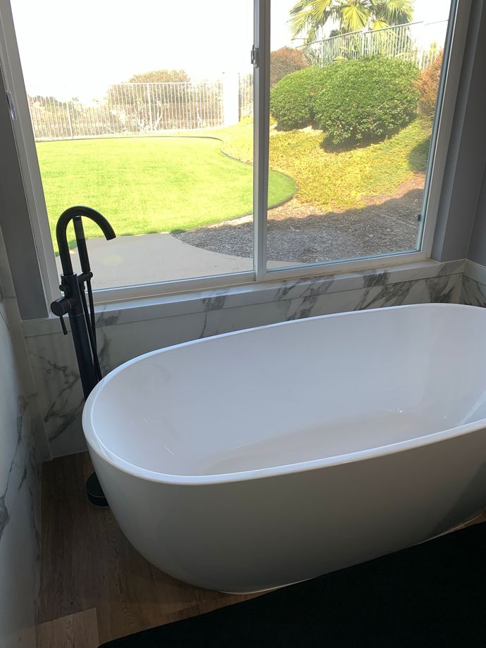 A white bathtub is sitting in front of a window in a bathroom.