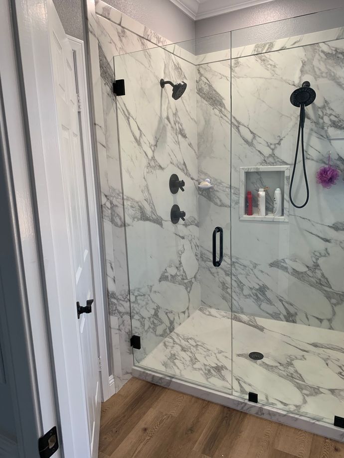 A bathroom with marble walls and a walk in shower with a glass door.